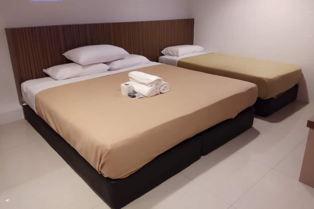 A hotel room with two beds, each with a brown bedspread and white pillows. There are towels and a small item on the bed.