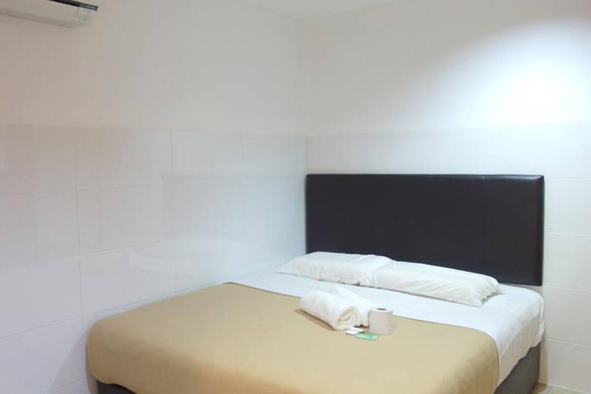 A small, clean room with a bed, a headboard, and a wall-mounted air conditioner.