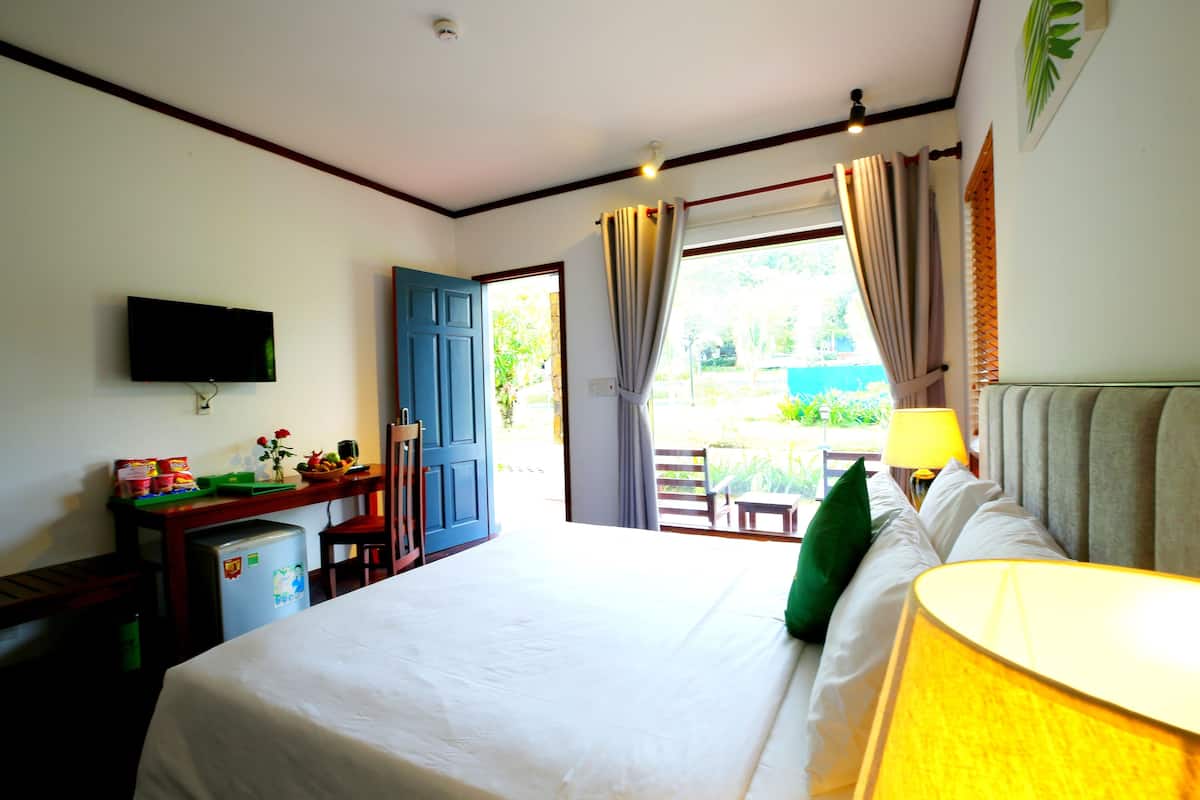 A hotel room with a bed, a desk with a computer, a TV, and a window with curtains.