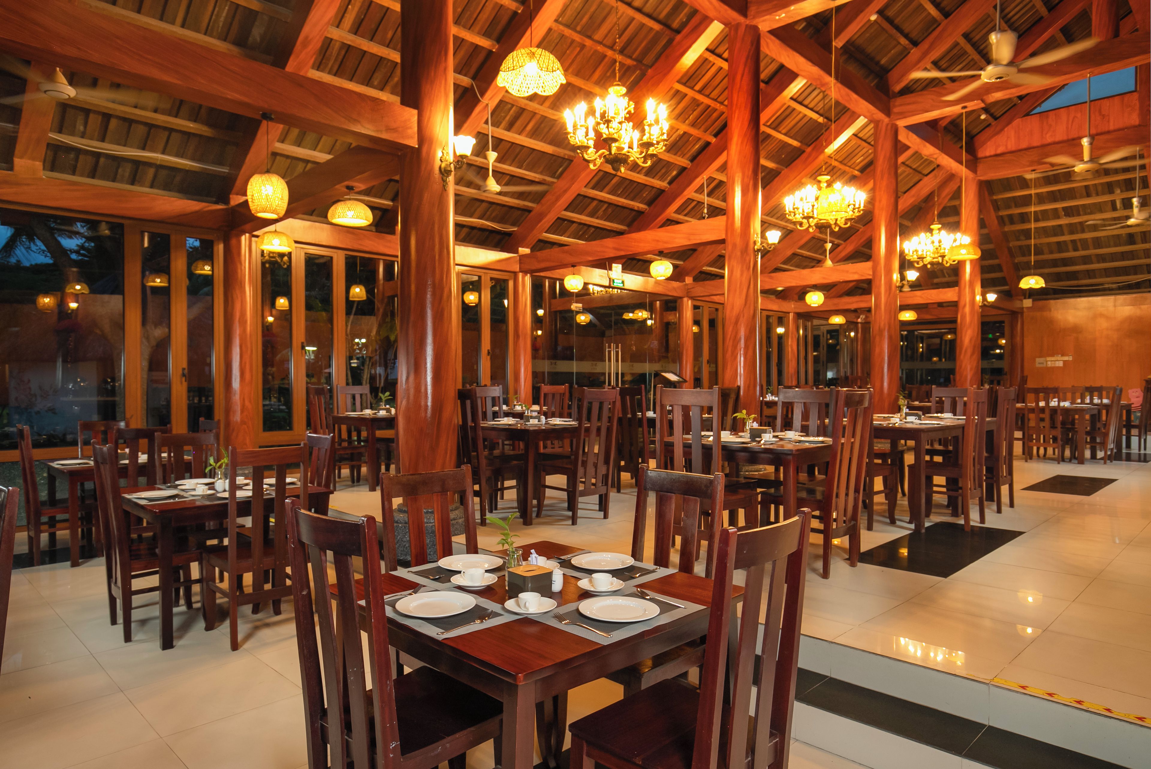 A restaurant with wooden beams, chandeliers, and tables set for dining.