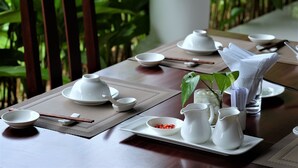 A dining table set with white dishes, chopsticks, and a pitcher, surrounded by greenery. - Santa Garden Resort (Phu Quoc)