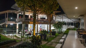 A multi-level outdoor dining area with tables and chairs, surrounded by greenery and a large tree. - D' Agape Meeting & Conference (Megamendung)