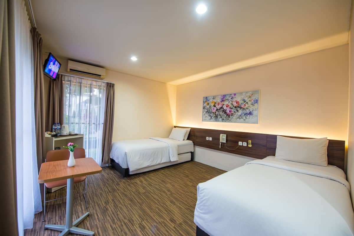 A hotel room with two beds, a desk with a vase of flowers, a television, and a painting on the wall.