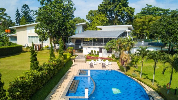A swimming pool with a tiled deck, surrounded by greenery and a building with a flat roof. - D' Agape Meeting & Conference (Megamendung)