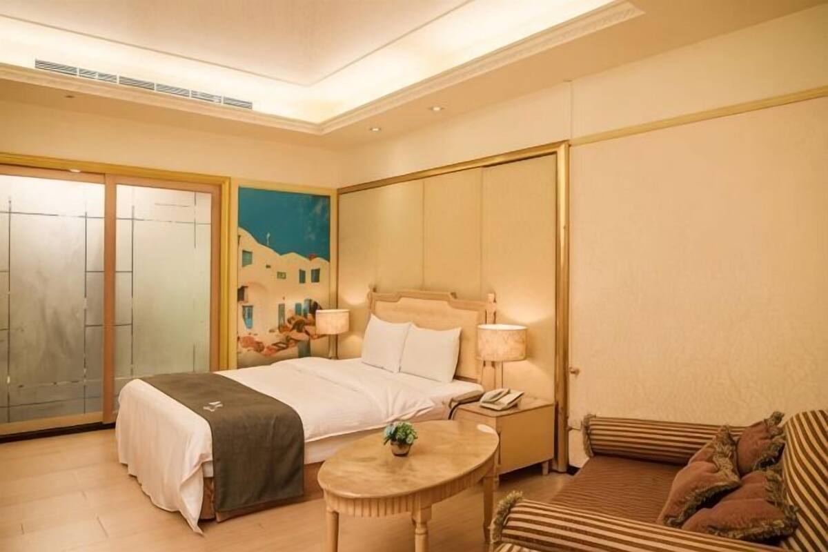 A hotel room with a bed, bedside table, lamp, and a small round table with a plant.