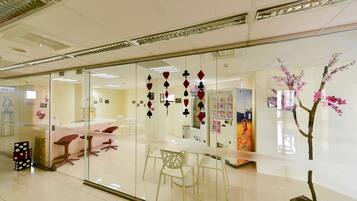 Un espacio de oficina moderno con separadores de vidrio, mobiliario blanco y elementos decorativos como tarjetas colgantes e instalación floral.