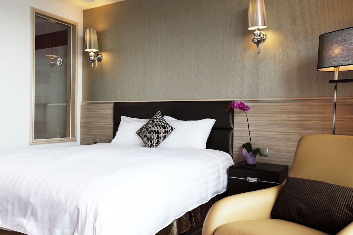 Una habitación de hotel con una cama grande, una mesita de noche, una lámpara y una silla.