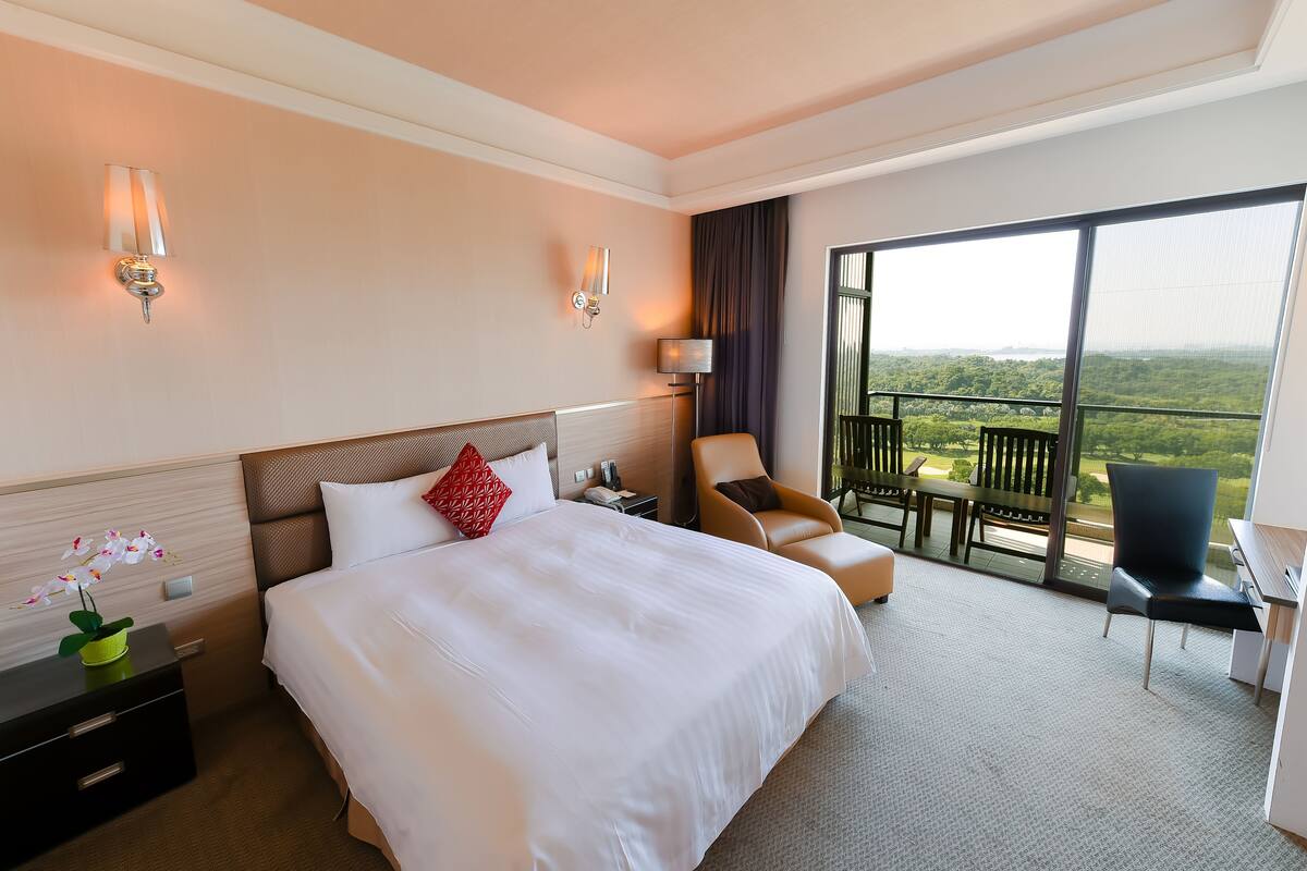 Habitación de hotel con una cama grande, un escritorio, una silla y un balcón con vistas.