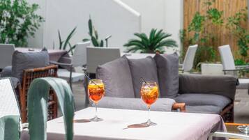 Un espace de détente moderne avec deux boissons sur une table, un canapé gris et diverses plantes en arrière-plan.