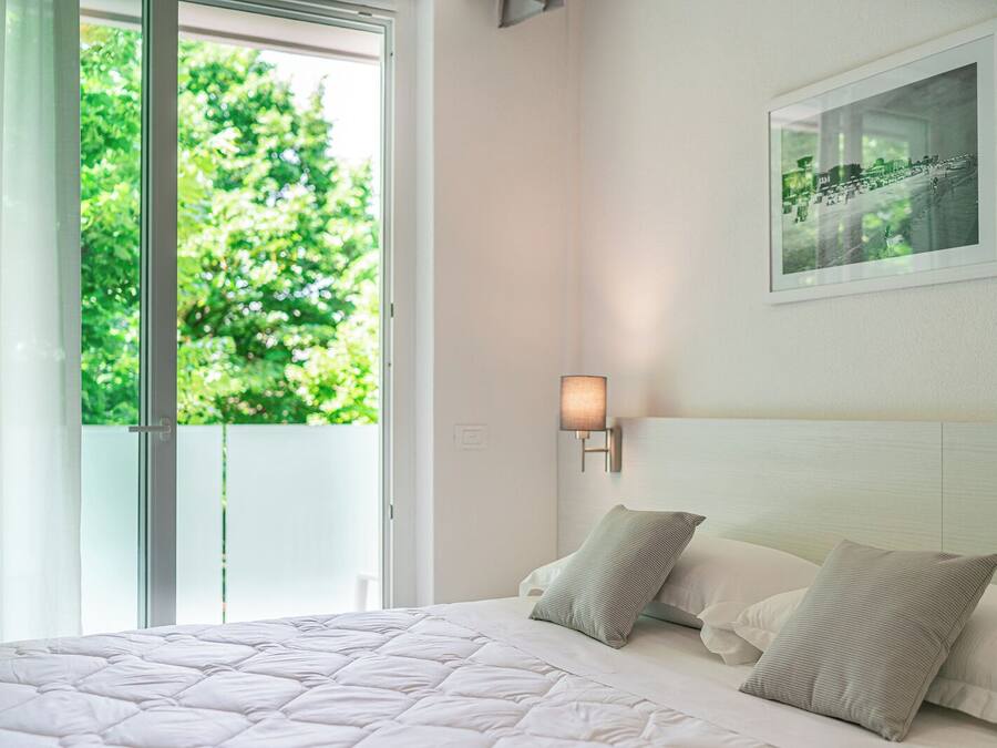 A bedroom with a bed, pillows, a nightstand, a wall-mounted lamp, and a framed picture.