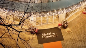 Entrada de un hotel con un cartel que dice "Hotel Centrale" y un árbol de Navidad decorado con luces y regalos.