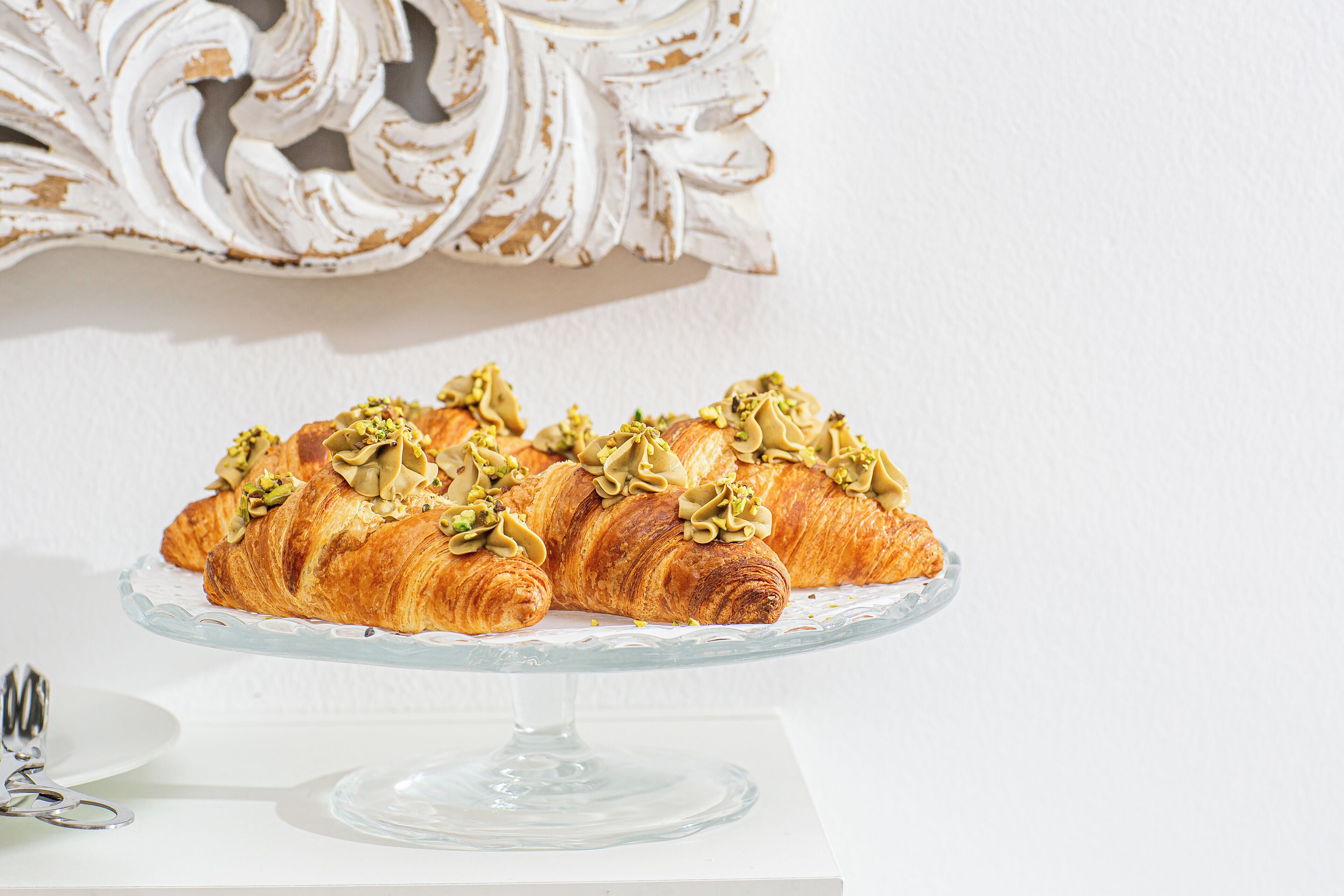 Un présentoir à gâteaux en verre, sur lequel reposent deux croissants garnis de noix et de crème.