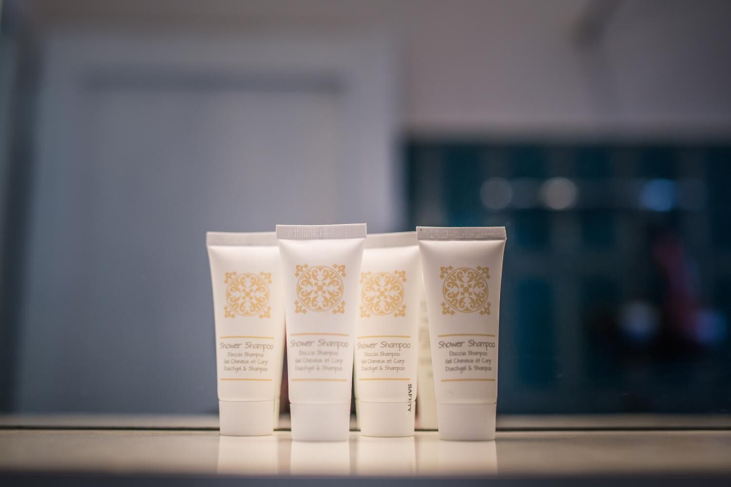 Quatre tubes de shampoing pour la douche, posés sur une surface réfléchissante.