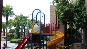 An outdoor play area with slides and climbing structures, surrounded by greenery and a building in the background. - Fabulous Service Suites At Times Square (Kuala Lumpur)