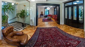 A spacious living area with a herringbone wooden floor, a red patterned rug, a leather armchair, and a view into the adjacent room with red sofas.