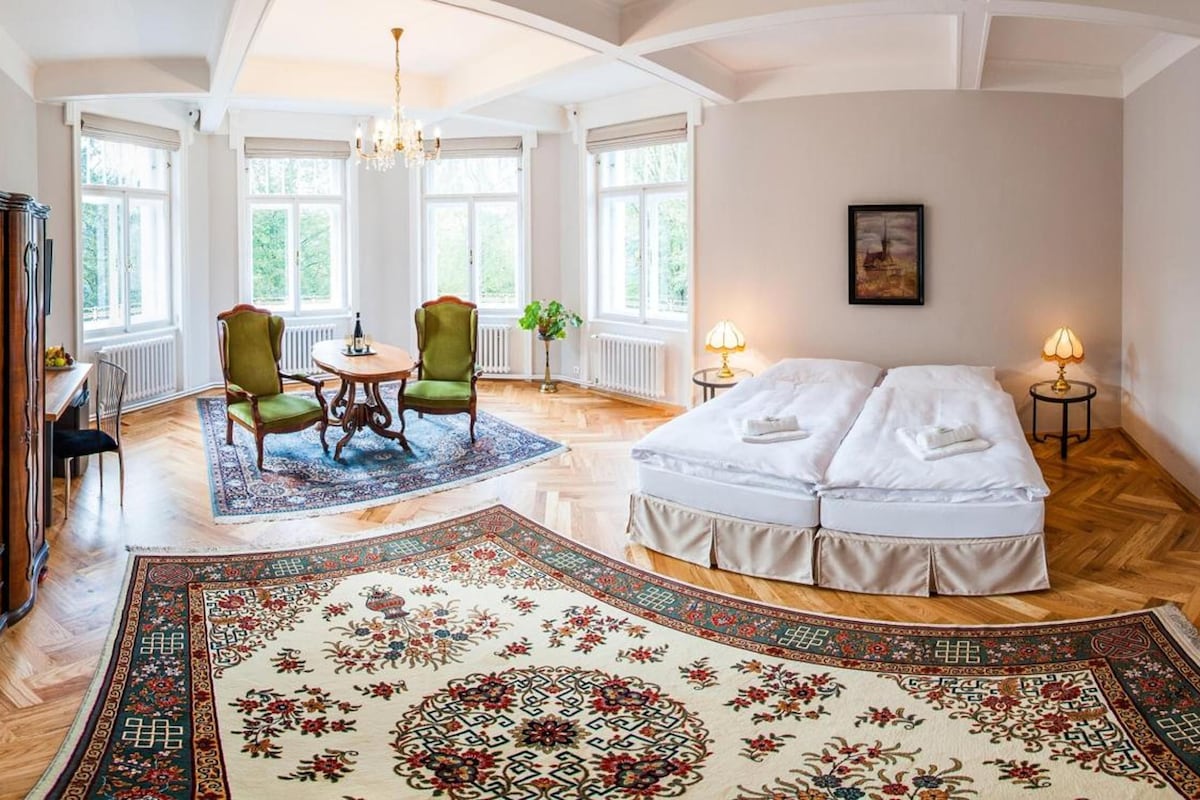 A spacious room with a large bed, a dining area with chairs, and a wooden cabinet.