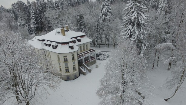 A snow-covered building with a symmetrical facade, multiple chimneys, and a central entrance.