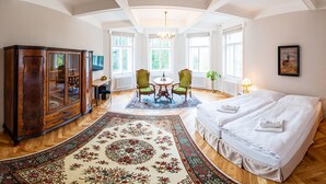 A spacious room with a large bed, a wooden cabinet, a dining table with chairs, and a chandelier.