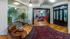 A spacious living area with a herringbone wooden floor, a large red patterned rug, a leather armchair, and a glass partition with plants.