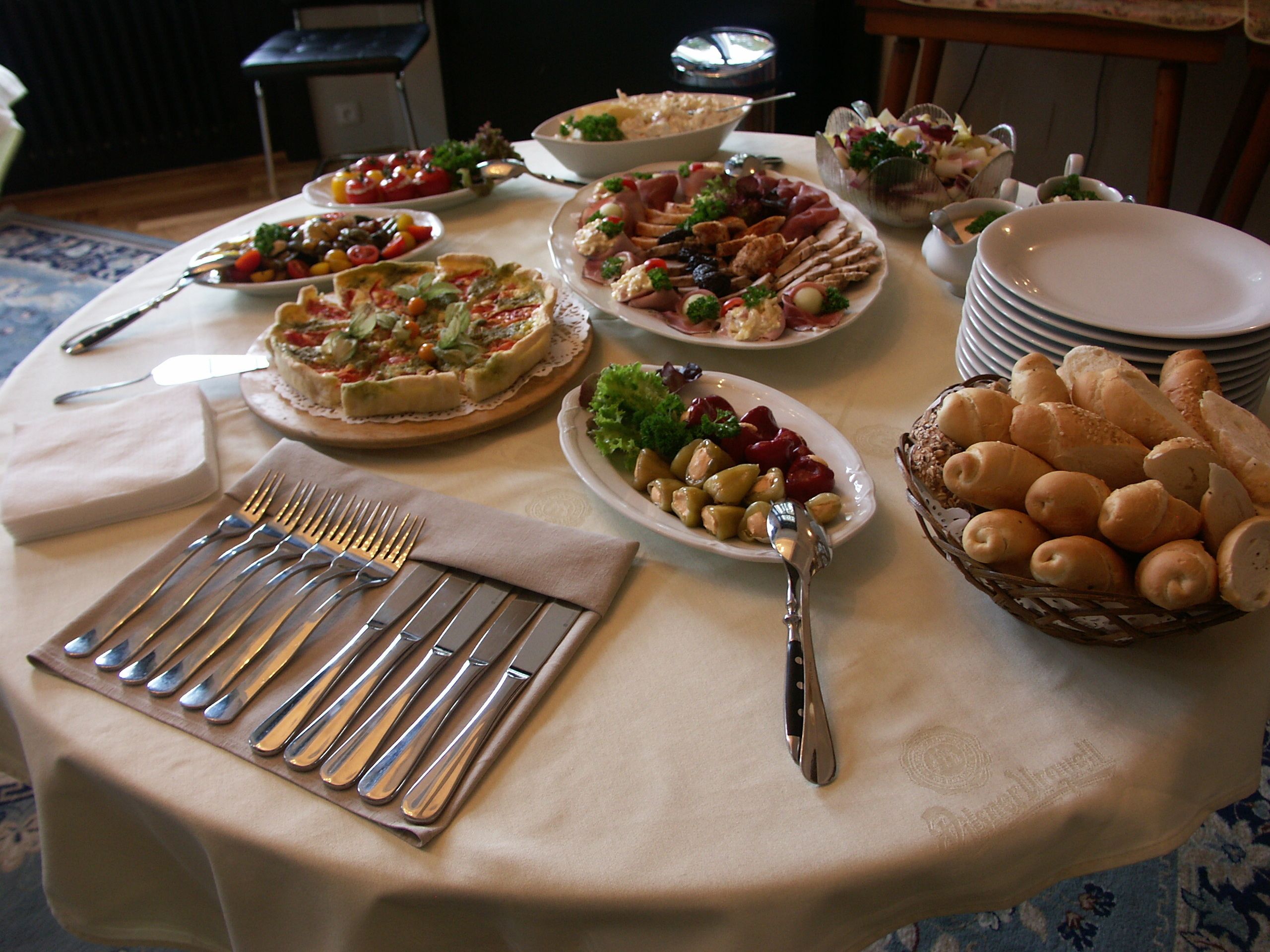 A table set with various dishes, including pizzas, salads, and bread, with cutlery and plates arranged for guests.