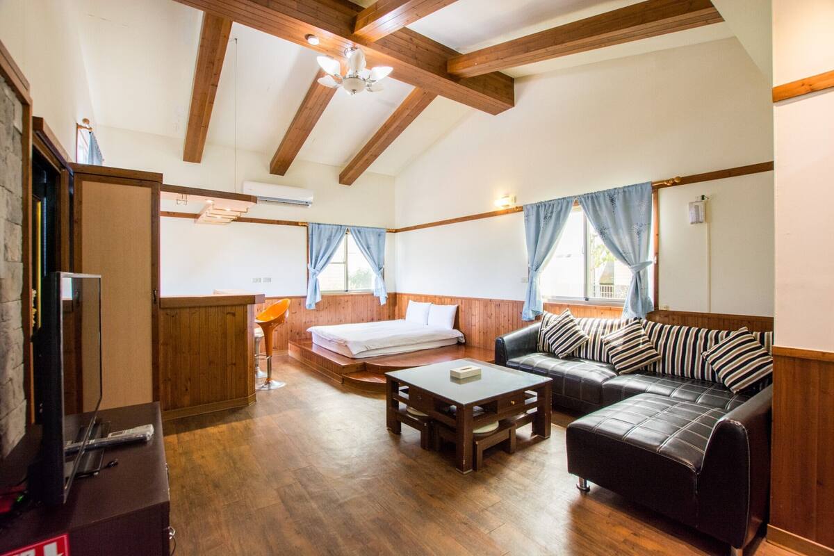 A room with a wooden ceiling, a sofa, a table, and a bed.