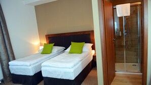 A hotel room with two single beds, a wooden headboard, a shower area, and a carpeted floor.