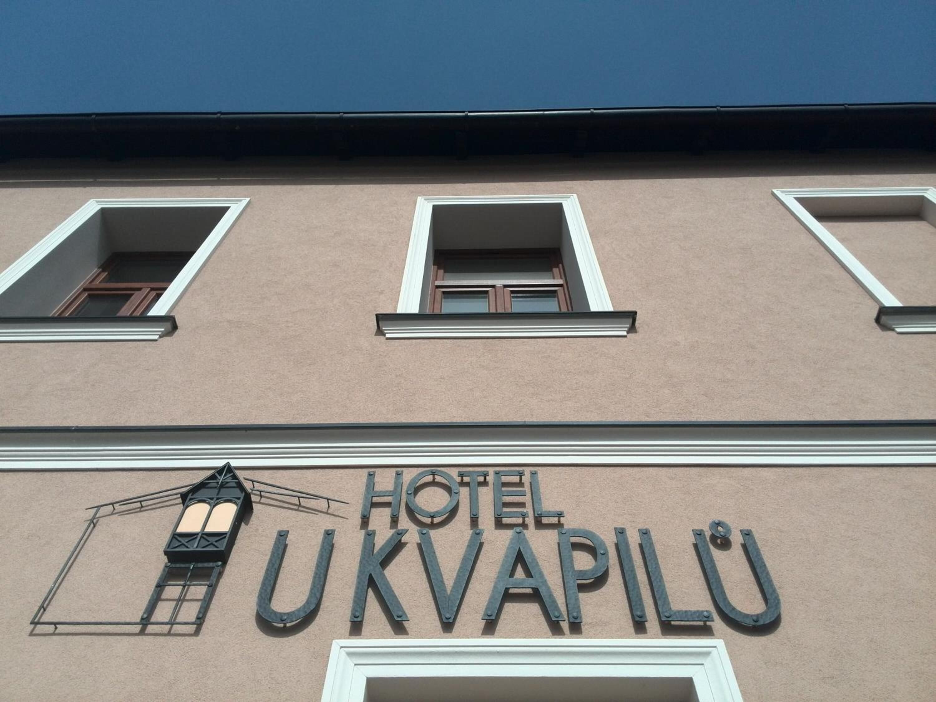 A building with a sign reading 'HOTEL UKVAPILU' and three windows with shutters.