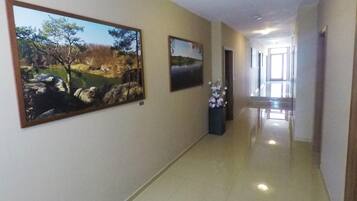 A hallway with two landscape paintings on the walls, a vase with flowers, and a view into another room.