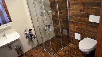 A bathroom with a glass shower enclosure, a white sink, and a toilet.
