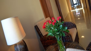 A wicker chair with a cushion, a vase with red flowers, and a lamp.