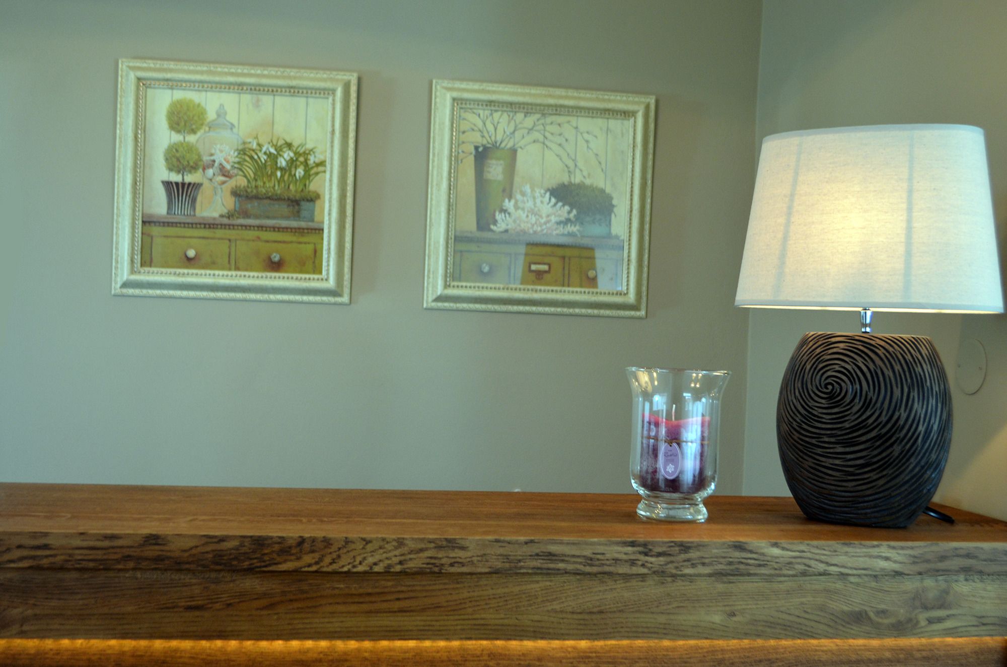 A wooden table with a lamp and two framed pictures on the wall.