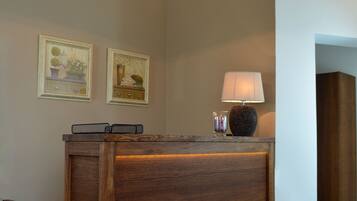 A reception desk with a wooden finish, a wall-mounted lamp, and two framed pictures.