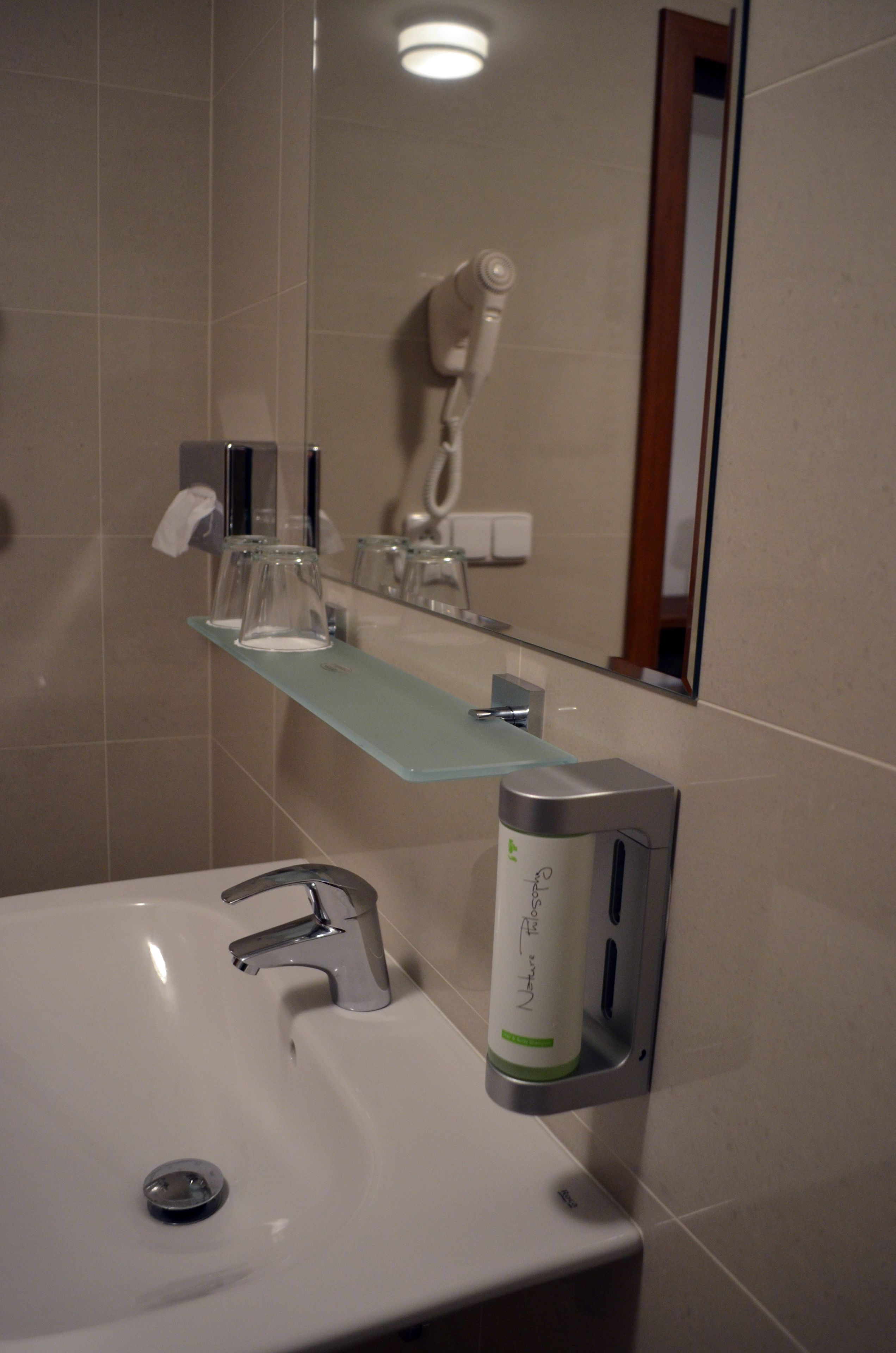 Een badkamer met een wit wastafelmeubel, een spiegel, een glazen plankje met toiletartikelen en een handdroger.