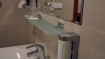 Een badkamer met een wit wastafelmeubel, een spiegel, een glazen plankje met toiletartikelen en een handdroger.