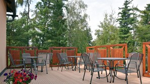 An outdoor patio with metal chairs and tables, surrounded by wooden fences and trees.
