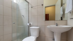 Et badeværelse med glasvæg omkring brusebad, toilet og håndvask.