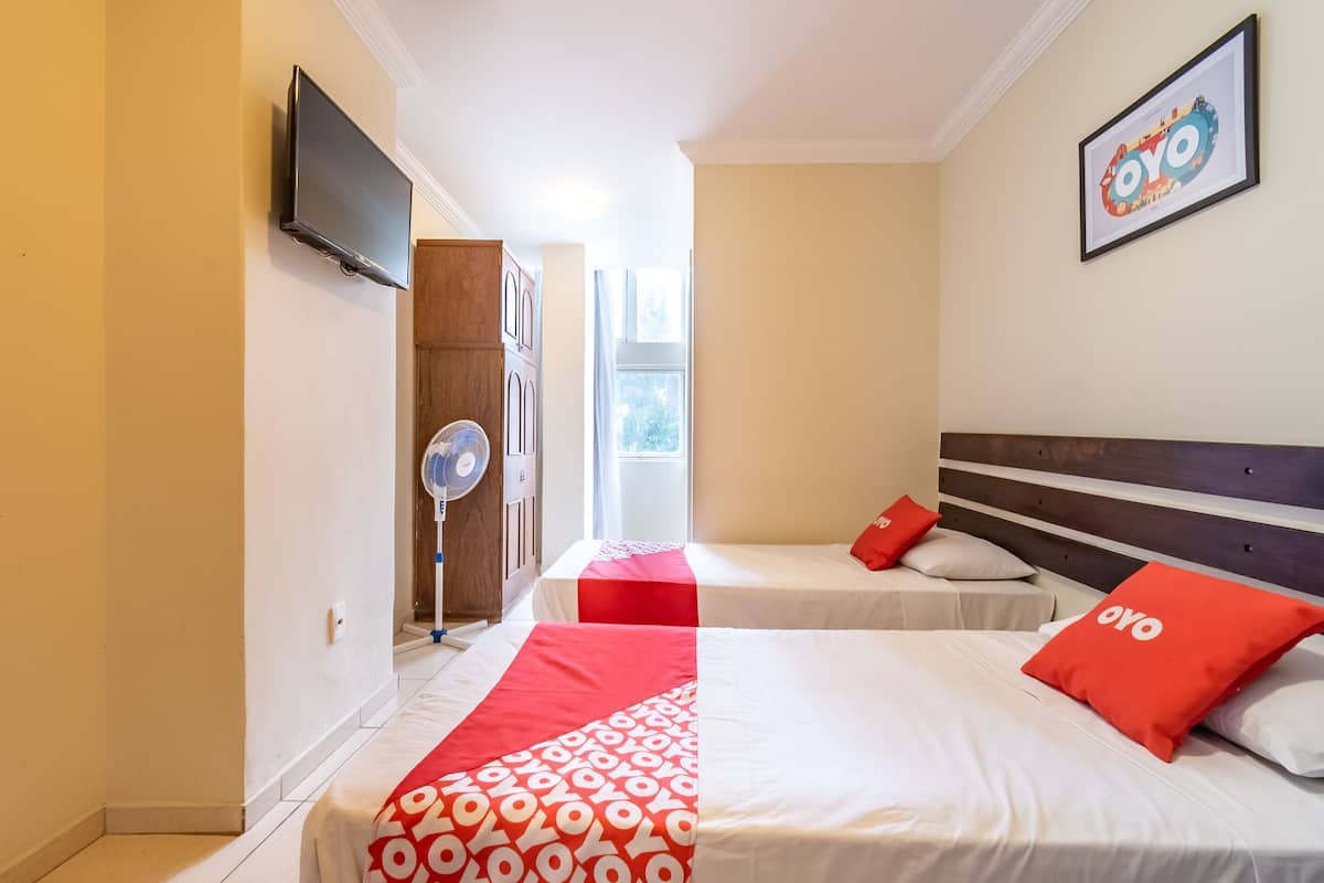 A hotel room with two beds, a TV, a fan, and a window.
