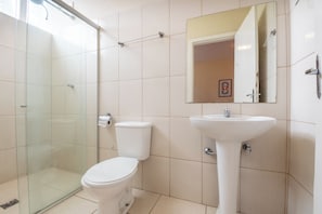 A bathroom with a glass shower enclosure, a toilet, and a pedestal sink with a mirror above it. - Hotel L'espace - Jaragua Belo Horizonte (Belo Horizonte)