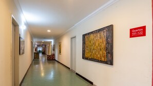 En hotellkorridor med ett grönt golv, inramade konstverk på väggarna och en skylt som visar rum nummer 101–122.