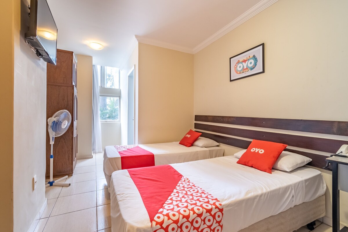 A hotel room with two beds, a TV, a fan, and a window.