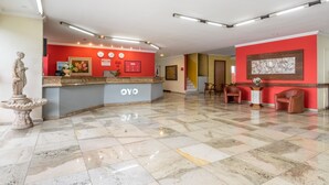 En hotellobby med ett marmorgolv, en receptionsdisk märkt med "OYO" och en staty till vänster.