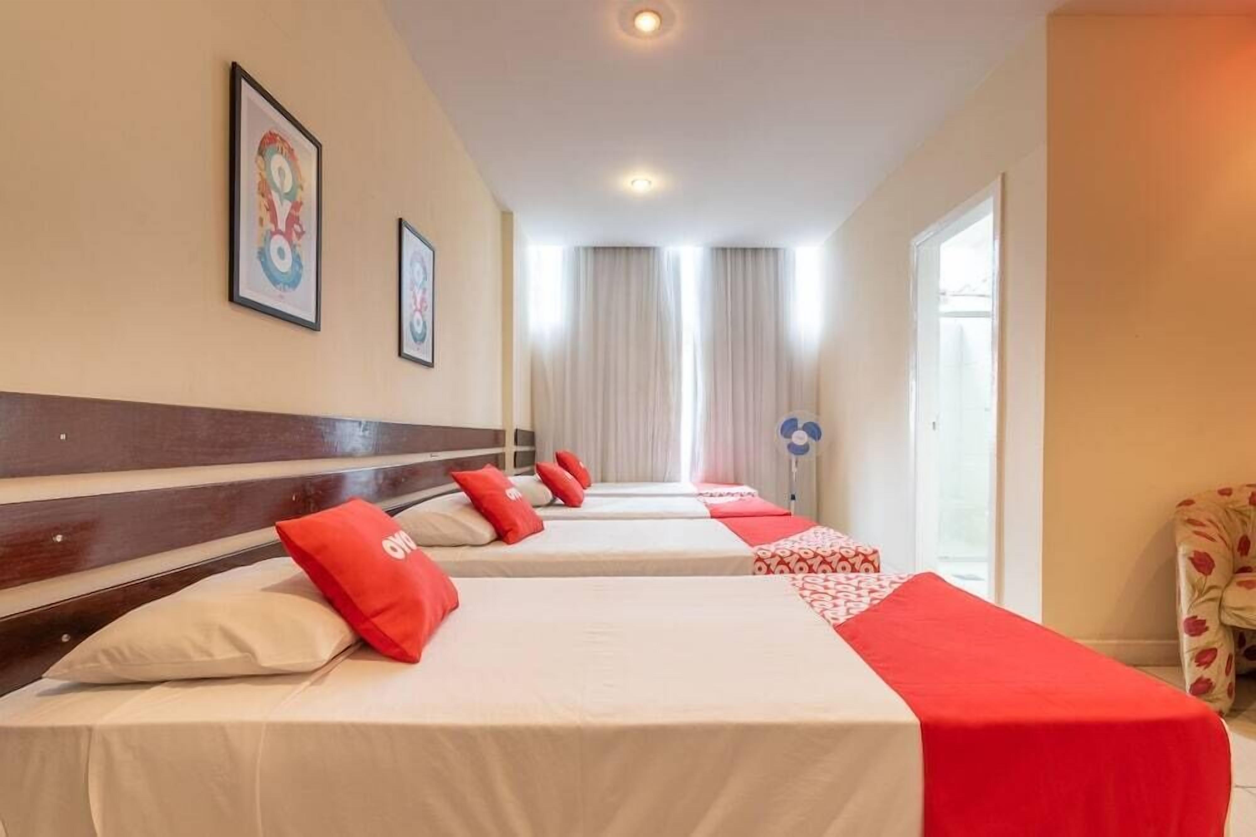 Ett hotellrum med fyra sängar placerade i en rad, ett trägaveltavla och inramade konstverk på väggarna.