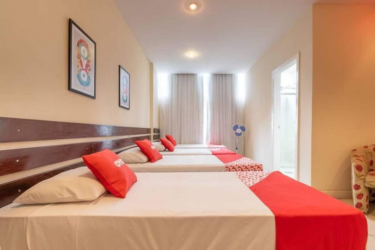 A hotel room with four beds aligned in a row, a wooden headboard, and framed artwork on the walls.