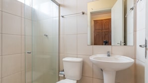 Et badeværelse med brusekabine i glas, et hvidt toilet og en hvid vask.