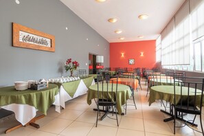 A dining area with tables set for a meal, chairs, and a vase of flowers. - Hotel L'espace - Jaragua Belo Horizonte (Belo Horizonte)