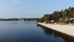 Un hôtel situé au bord d’un lac, avec une plage de sable, des bateaux et une colline boisée.