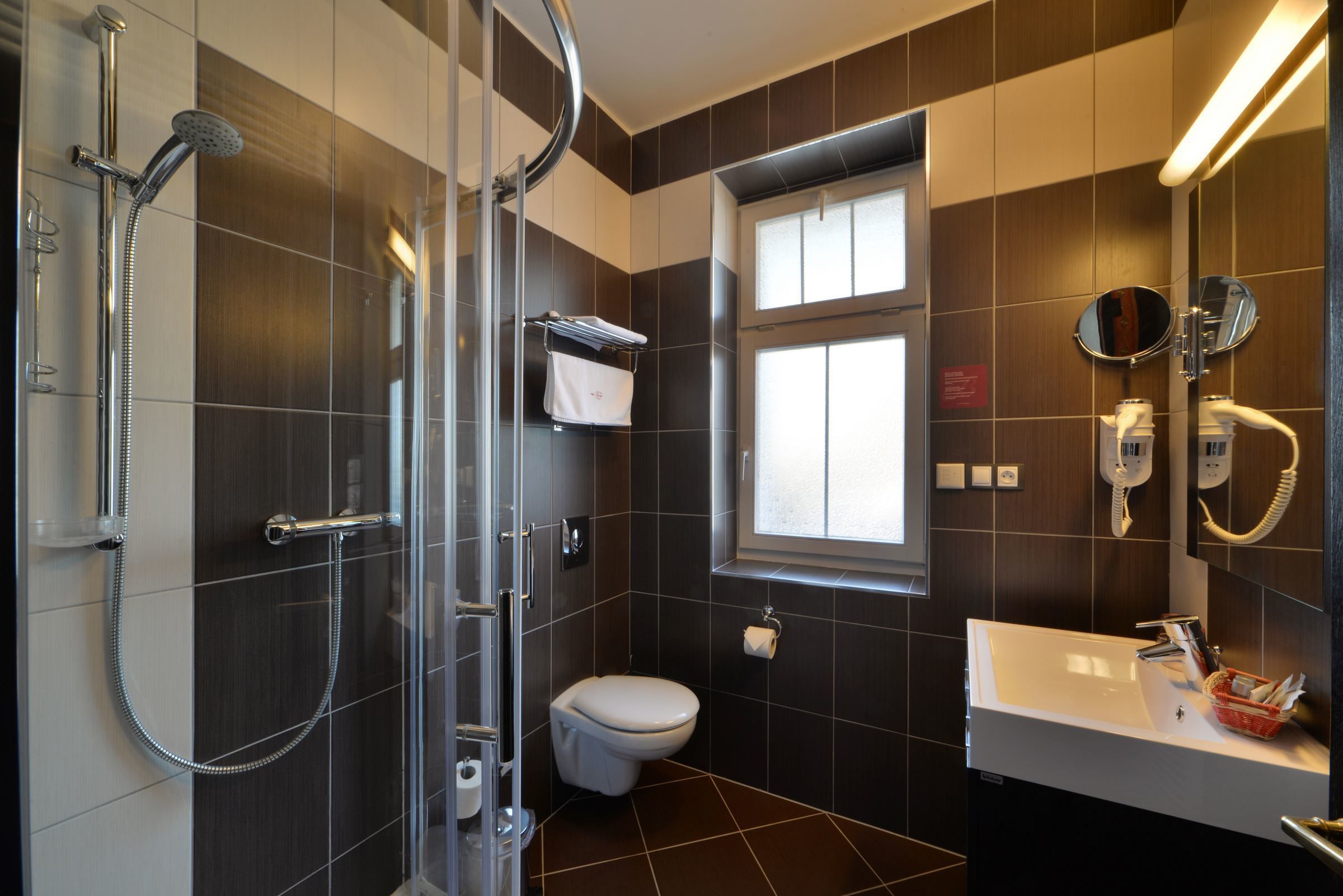 A modern bathroom with a glass shower enclosure, a toilet, a sink with a mirror, and a window providing natural light.