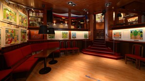 Un restaurant avec un plafond en bois, des sièges rouges et des œuvres d’art accrochées aux murs.