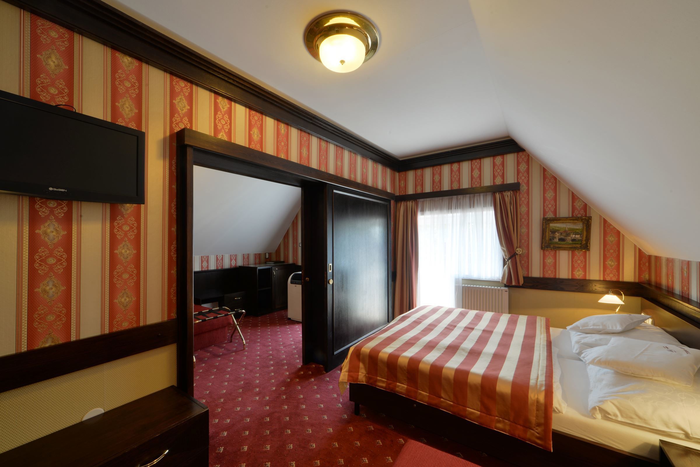 A hotel room with a bed, a desk, a chair, a wardrobe, and a television.