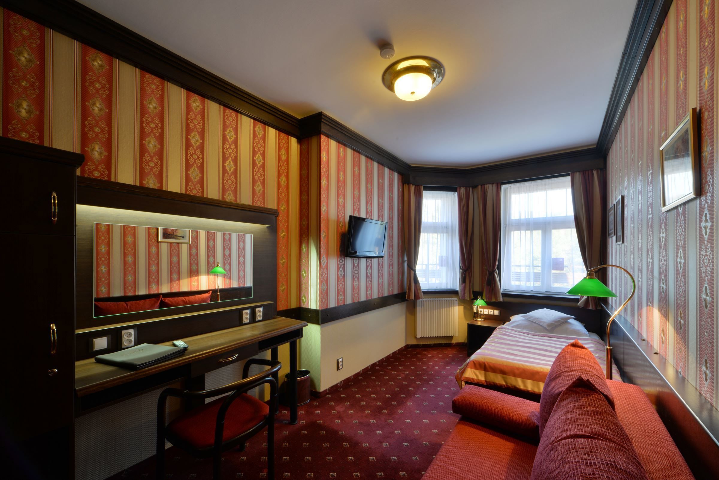 A hotel room with a bed, a desk, a chair, a television, and a window with curtains.